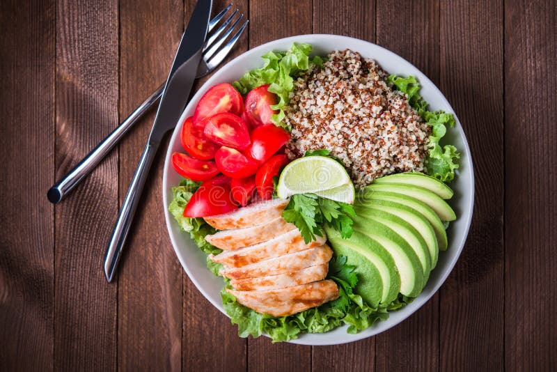 Healthy salad bowl with quinoa, tomatoes, chicken, avocado, lime and mixed greens, lettuce, parsley