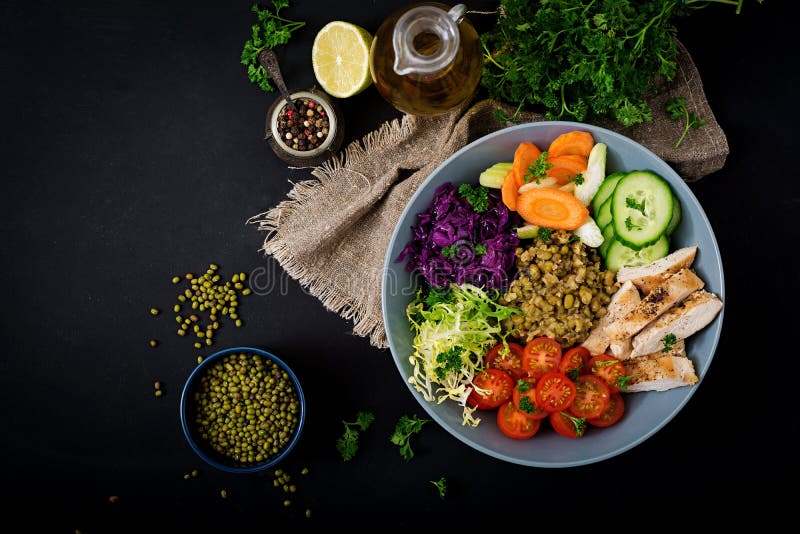 Healthy salad with chicken, tomatoes, cucumber, lettuce, carrot, celery, red cabbage and mung bean on dark background