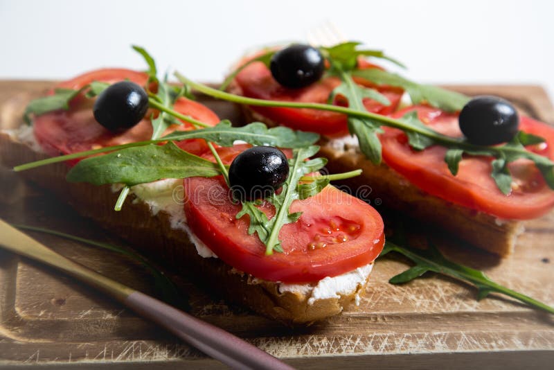 Healthy snack or Tomato, arugula, olives and creamy cheese on toast bread. Organic breakfast