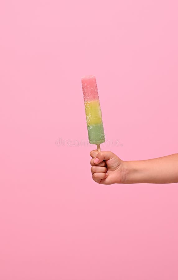 Healthy vegan ice cream popsicle in hand of a baby girl with pink wall at background with copy space . Summer dessert and cheerful