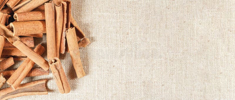 Heap of cinnamon bark sticks on linen tablecloth. Wide banner with empty space for text right side.