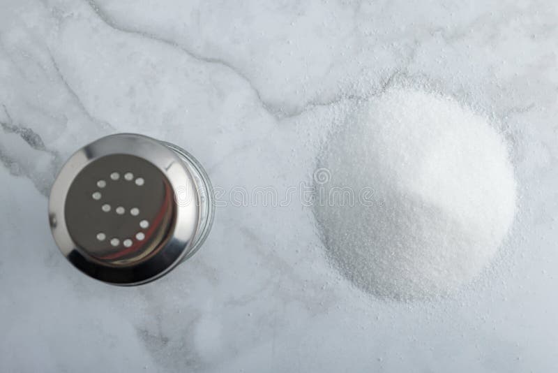 Heap of fine salt and salt shaker and a h on marble countertop royalty free stock photography