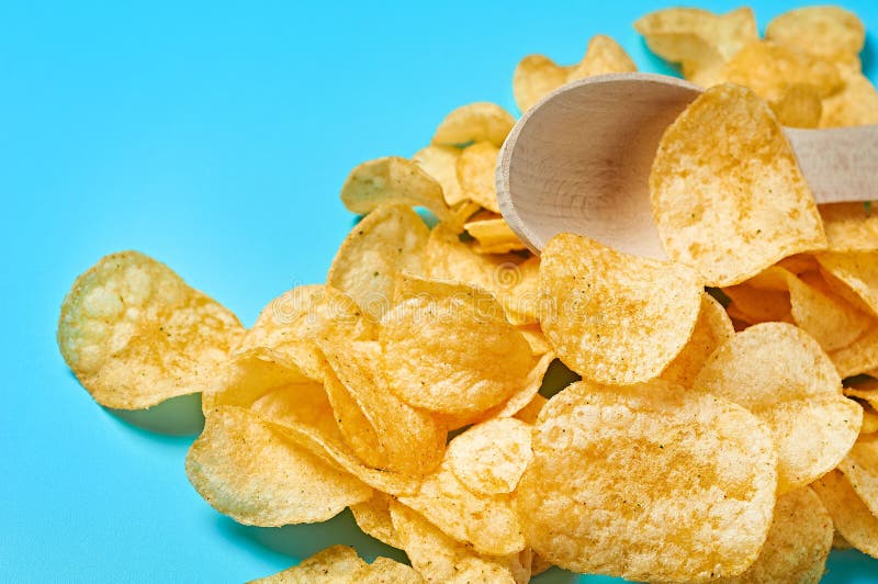 Heap of spicy fried potato chips and wooden spoon on blue background stock photography Heap of spicy fried potato chips and wooden spoon on blue background stock photography