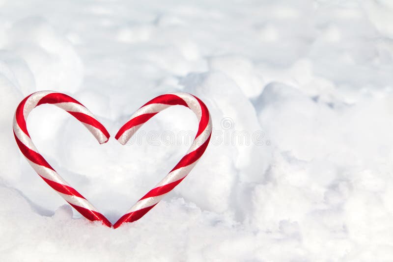 Two candy canes made into a heart shape in the snow with copy space. Two candy canes made into a heart shape in the snow with copy space.