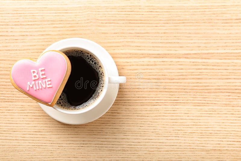 Heart shaped cookie with written phrase Be Mine and cup of coffee on wooden background, top view