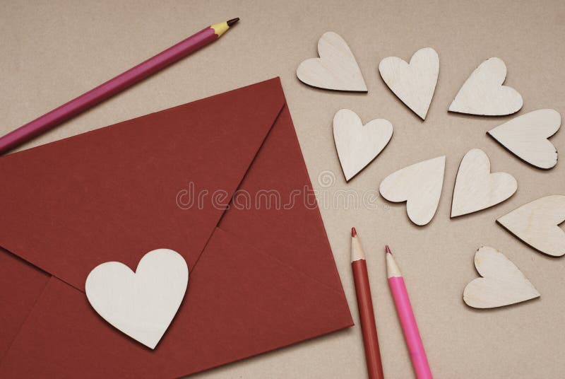 A heart shaped Valentine& x27;s Day card in a red envelope, surrounded by wooden hearts and colored pencils.