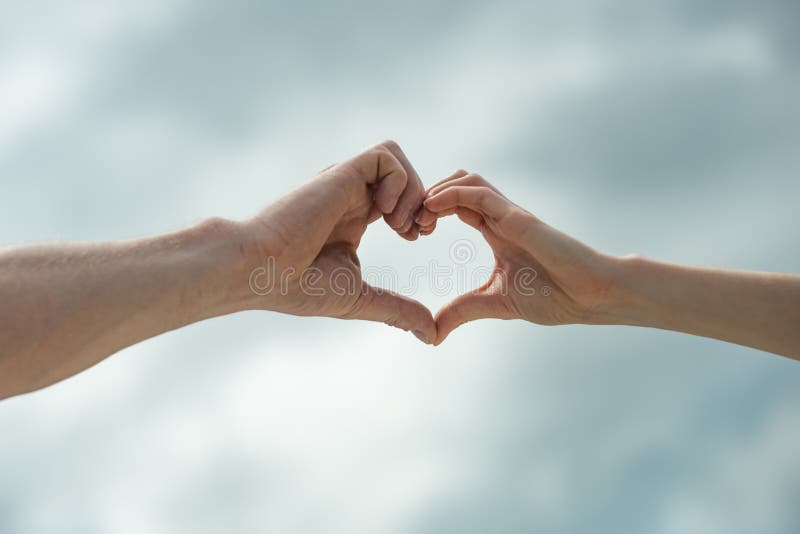 Heart sign. Hands show a heart symbol on sky background. Love. Man and woman. Partnership. Gender Equality. Love between stock image Heart sign. Hands show a heart symbol on sky background. Love. Man and woman. Partnership. Gender Equality. Love between stock image