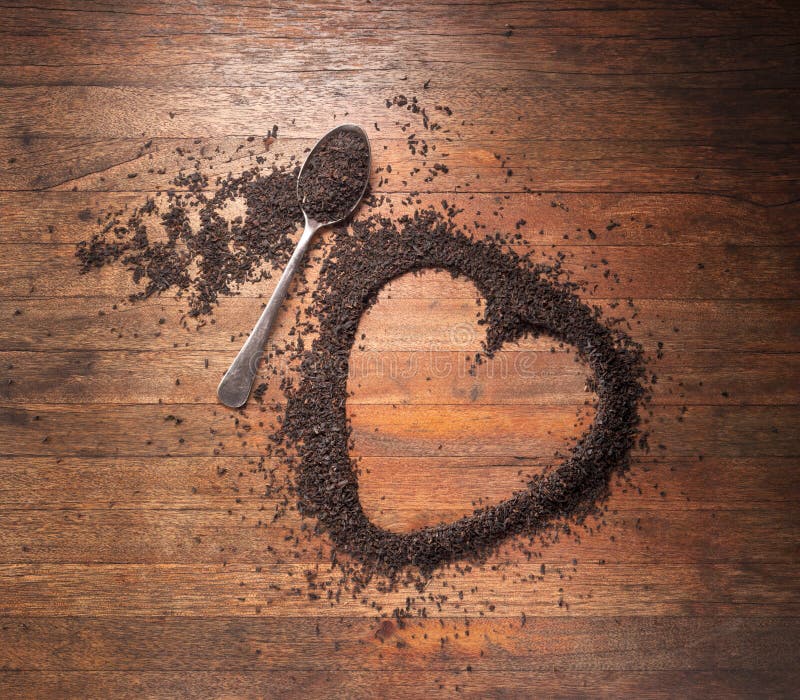 Srdce tvaru vyrobené s čierny čaj s lyžička na rustikálne drevené pozadí fotografoval z vyššie.