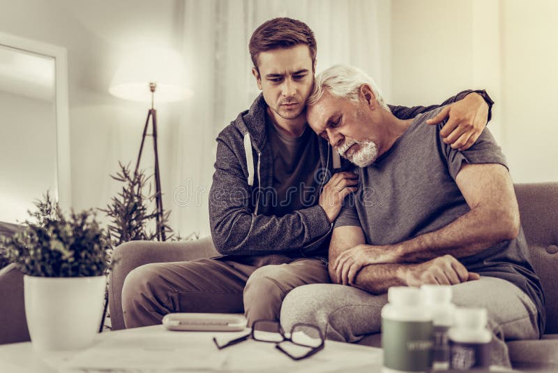 Heartsore wnuk ściska jego starszego srebrnowłosego dziadka i pociesza obraz stock Heartsore wnuk ściska jego starszego srebrnowłosego dziadka i pociesza obraz stock