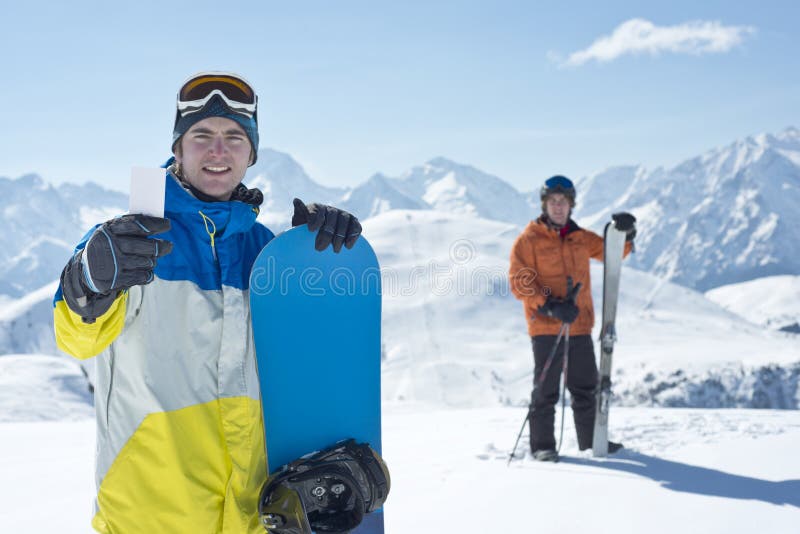 Two men with winter sport equipment looking at camera. One is showing a blank lift pass. Concept to illustrate ski admission fee. Two men with winter sport equipment looking at camera. One is showing a blank lift pass. Concept to illustrate ski admission fee