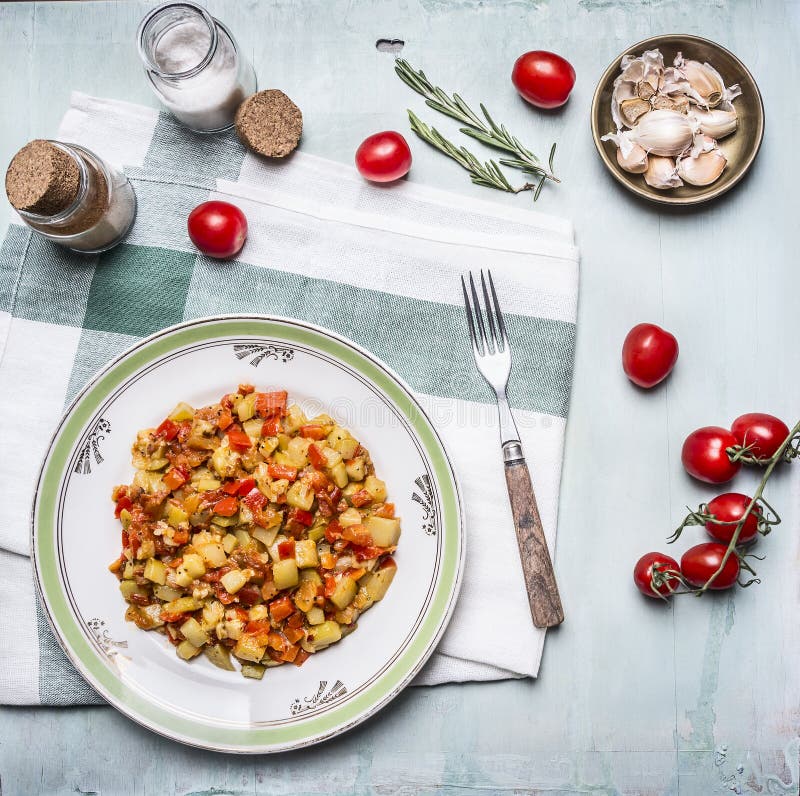 Heerlijke plantaardige hutspot in een witte plaat met een vork, met kruiden, knoflook en tomaten op een tak, op een servet op bla stock afbeelding Heerlijke plantaardige hutspot in een witte plaat met een vork, met kruiden, knoflook en tomaten op een tak, op een servet op bla stock afbeelding