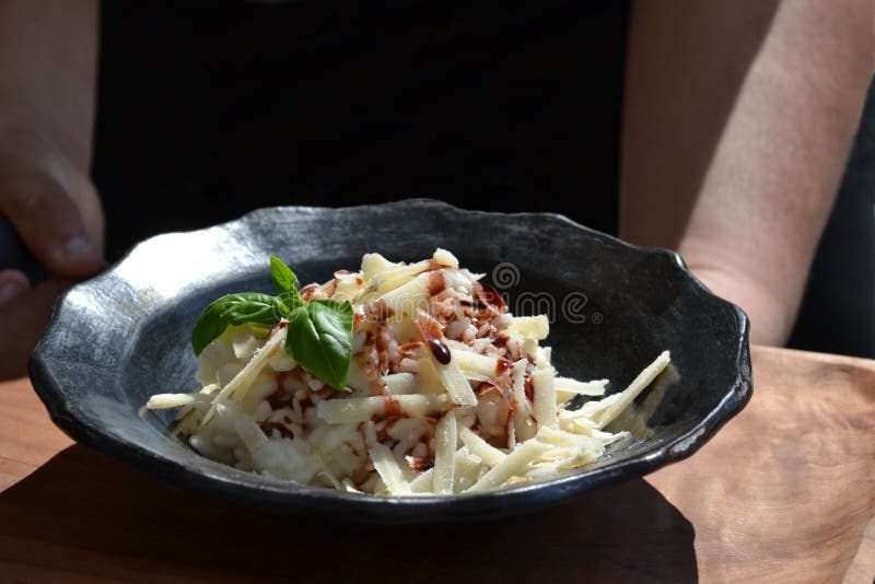 Heerlijke risotto op de zwarte ceramische die plaat met geschoren kaasparmezaanse kaas, peterselie en balsemieke azijn wordt bede royalty-vrije stock afbeelding Heerlijke risotto op de zwarte ceramische die plaat met geschoren kaasparmezaanse kaas, peterselie en balsemieke azijn wordt bede royalty-vrije stock afbeelding