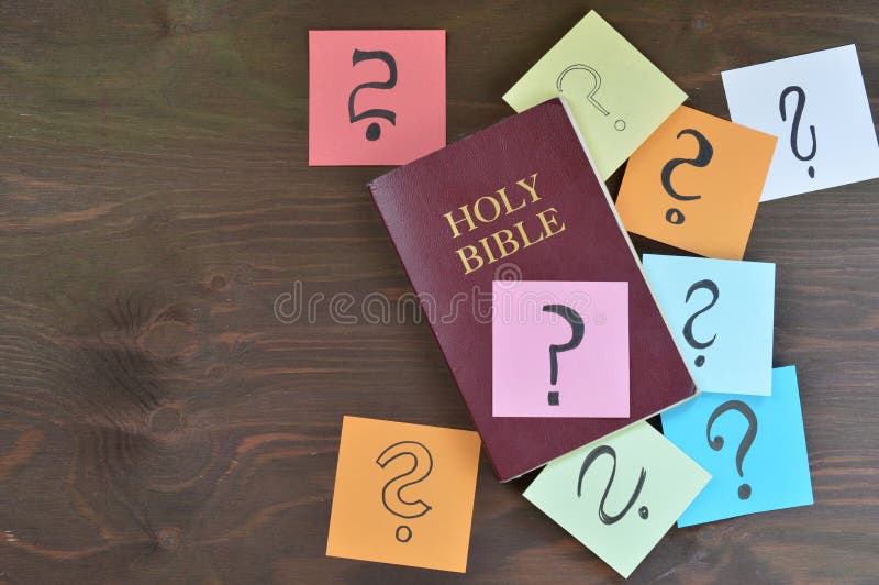 Holy bible and colorful note pads with question marks on brown wooden background as symbol for answers you can find in the bible or passages you don`t understand. Holy bible and colorful note pads with question marks on brown wooden background as symbol for answers you can find in the bible or passages you don`t understand