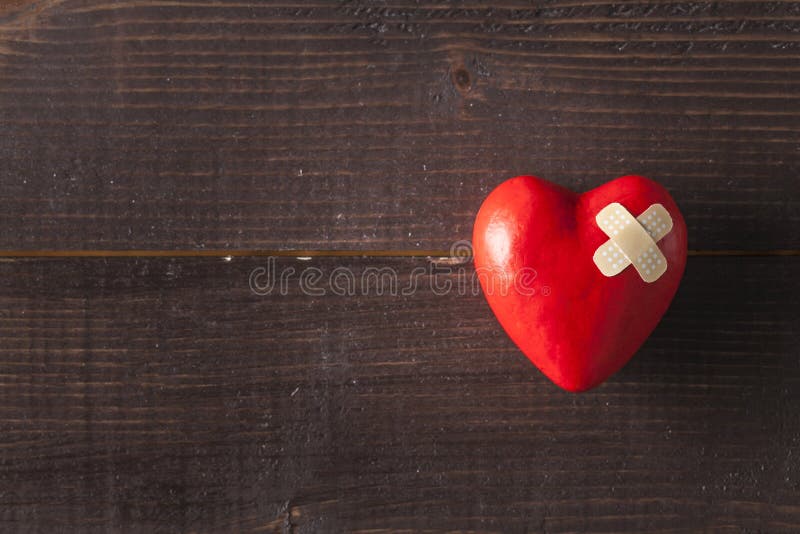 Red broken heart with a band-aid on a wooden background. Red broken heart with a band-aid on a wooden background