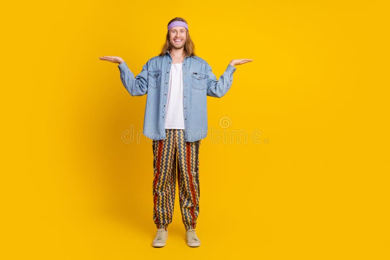 Full body photo of attractive young hippie man compare empty space wear trendy denim outfit isolated on yellow color background. Full body photo of attractive young hippie man compare empty space wear trendy denim outfit isolated on yellow color background.