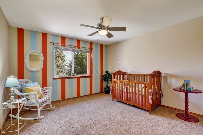 Bright colorful nursery room with contrast striped wall . The room is furnished with a crib, wicker rocking chair and a small table. Northwest, USA. Bright colorful nursery room with contrast striped wall . The room is furnished with a crib, wicker rocking chair and a small table. Northwest, USA