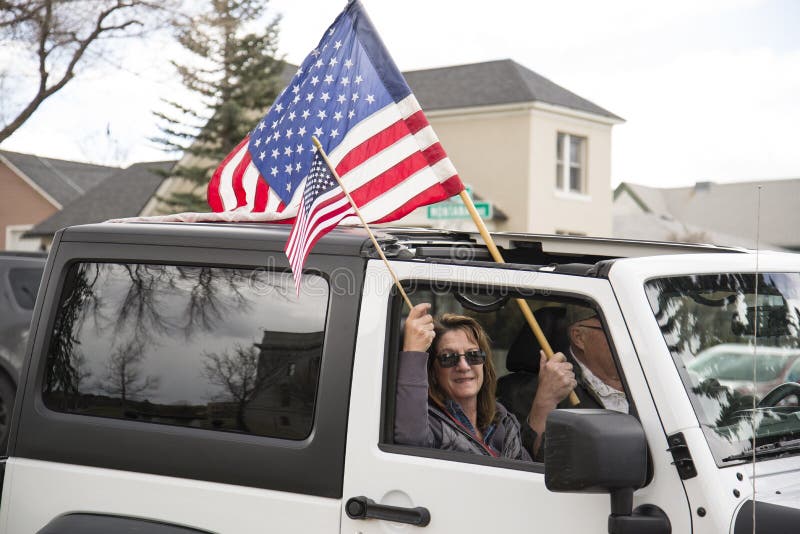 Helena, Montana - 19 april 2020: Man en vrouw houden Amerikaanse vlaggen in een witte jeep bij een vrijheidsdemonstratie rond het stock foto Helena, Montana - 19 april 2020: Man en vrouw houden Amerikaanse vlaggen in een witte jeep bij een vrijheidsdemonstratie rond het stock foto