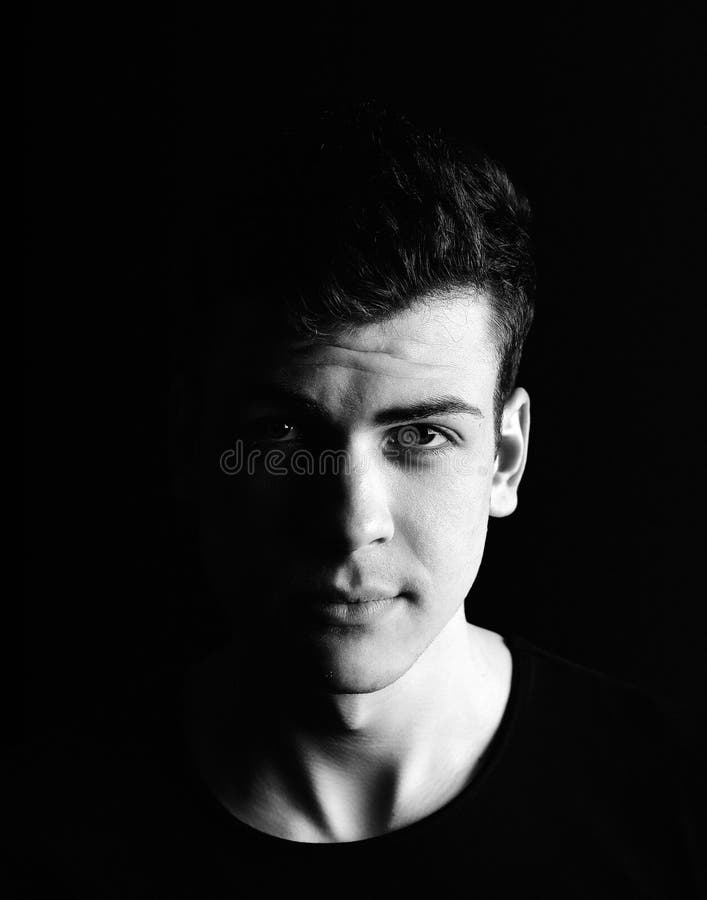 Photo of a young man in low-key style with a shadow on the half of the face. Studio photography with a hard light. Photo of a young man in low-key style with a shadow on the half of the face. Studio photography with a hard light.
