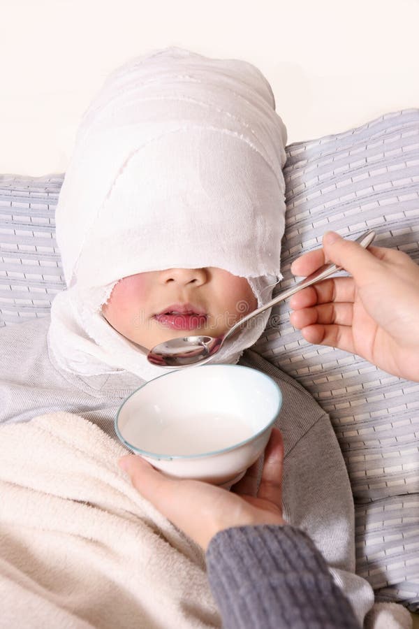 Un po ' di asian boy, con la testa quasi completamente vestita con un bendaggio, viene alimentata la medicina da qualcun altro.