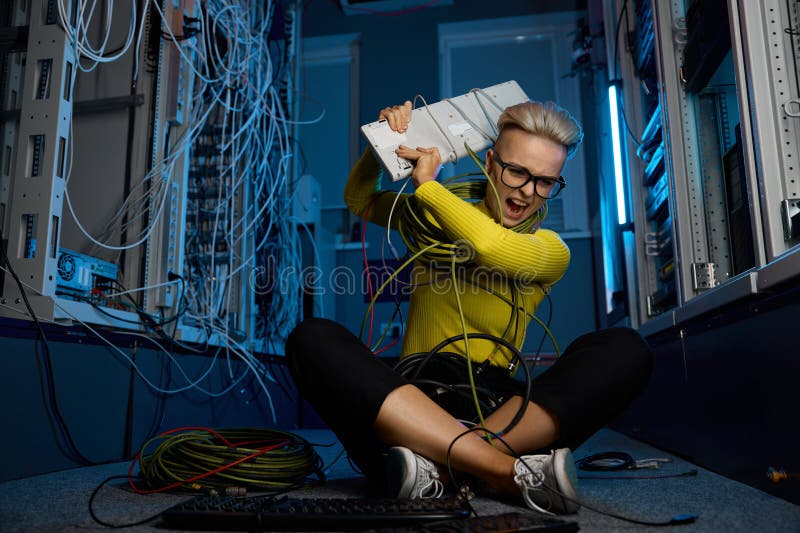 Hembra enojada frustrada técnica de TI lanzando el teclado de la computadora a la sala de servidores foto de archivo