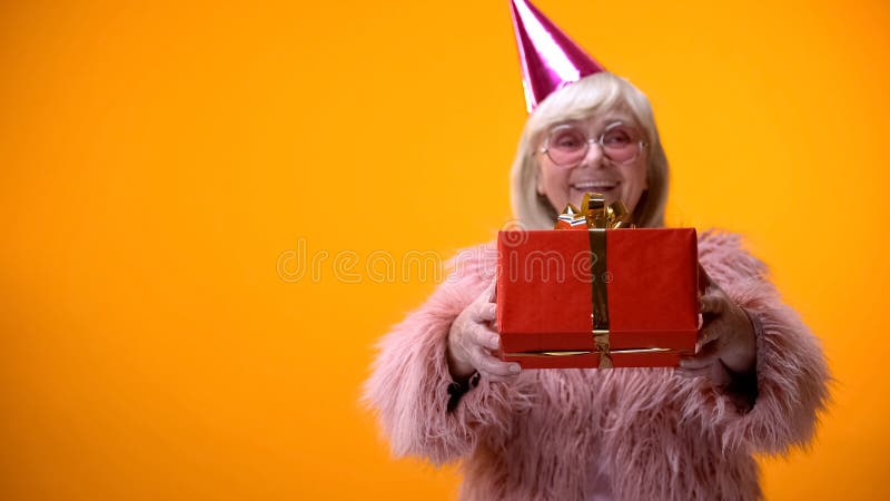 Hembra mayor alegre en la ropa divertida que da el regalo de cumplea?os, celebraci?n fotografía de archivo libre de regalías Hembra mayor alegre en la ropa divertida que da el regalo de cumplea?os, celebraci?n fotografía de archivo libre de regalías