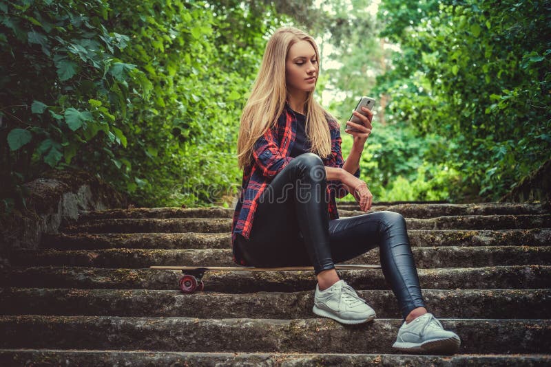 Hembra rubia casual con longboard usando smartphone imagen de archivo libre de regalías Hembra rubia casual con longboard usando smartphone imagen de archivo libre de regalías