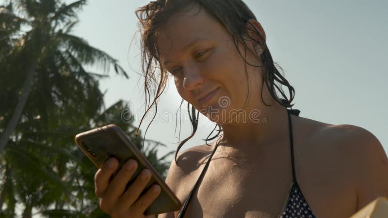 Hembra usando smartphone negro sobre fondo de palmera