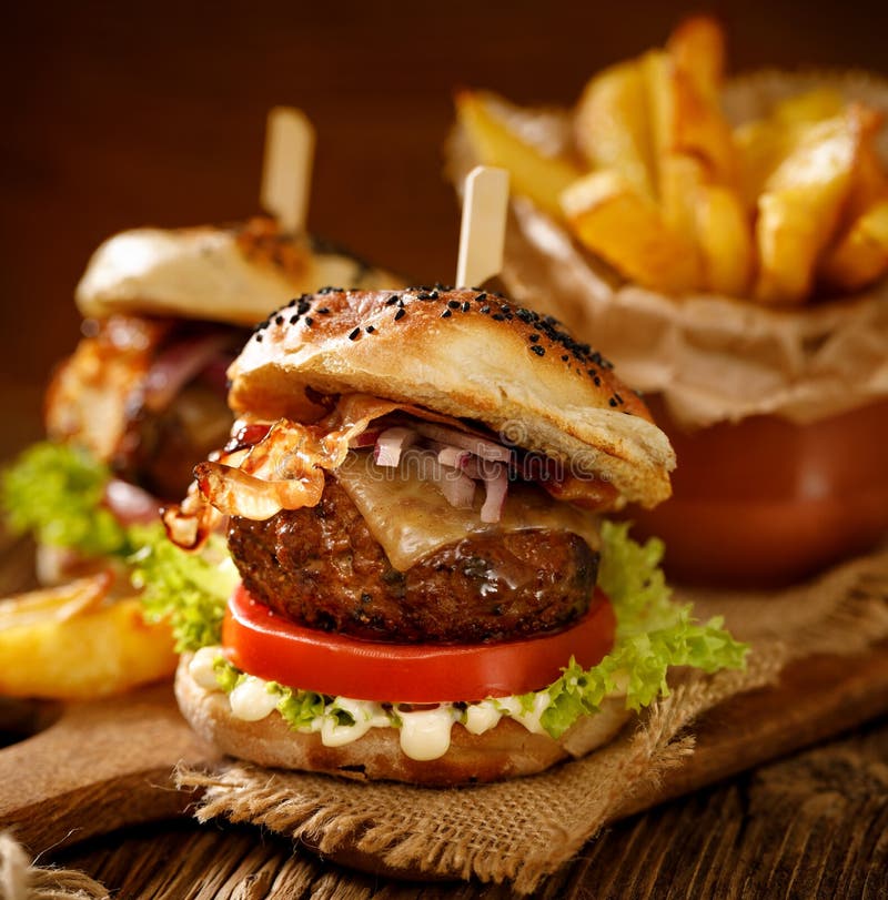 Hemlagade hamburgare med grillad bacon, den röda löken, ny grönsallat, gurkaknipor, tomaten och aromatisk majonnässås på ett trä royaltyfri foto Hemlagade hamburgare med grillad bacon, den röda löken, ny grönsallat, gurkaknipor, tomaten och aromatisk majonnässås på ett trä royaltyfri foto