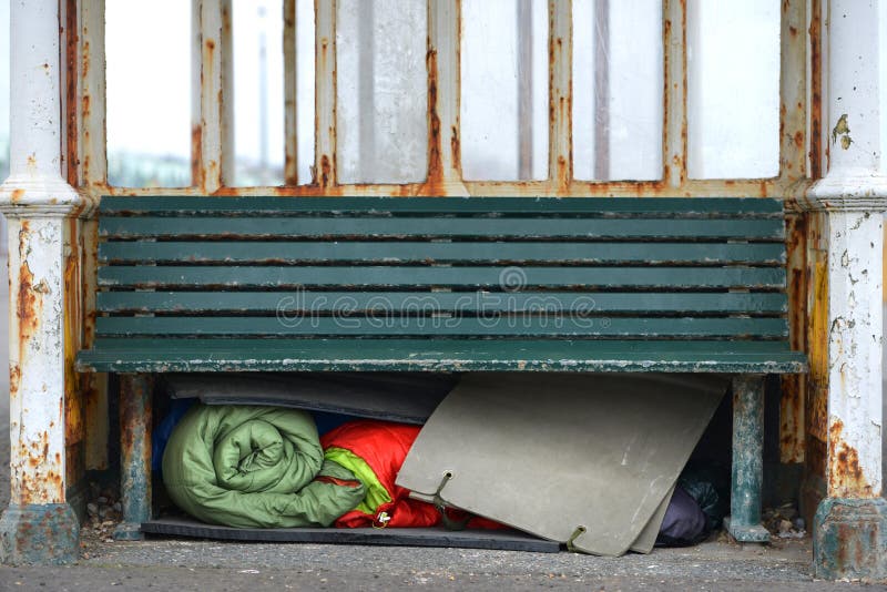 Homeless person`s sleeping bags and bedding under a bench. Homeless person`s sleeping bags and bedding under a bench