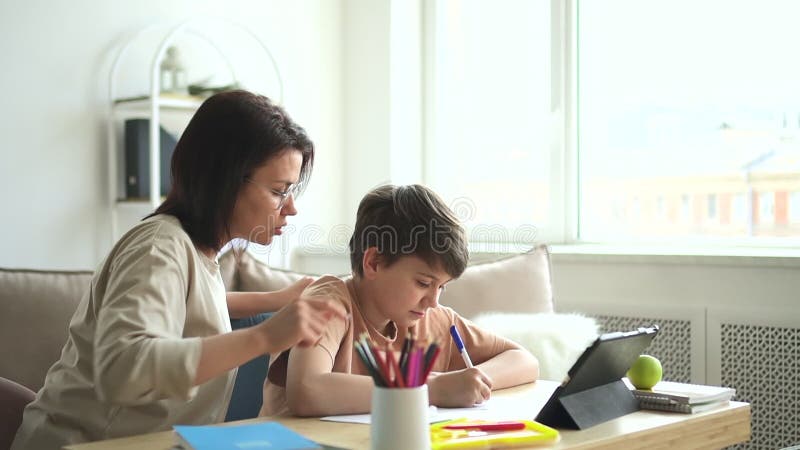 Hemlösa : skolpojke som skriver i anteckningsboken och pratar med mamma som sitter på bord. stock video