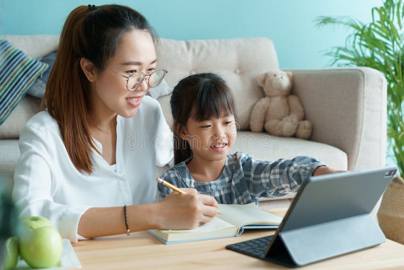 Hemmakolering. en familj med dotter som gör läxor genom att använda en tablett med hjälp av modern. asiatisk mamma och barn kan lä arkivbilder