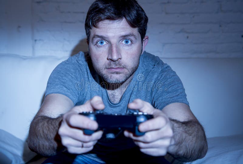 Hemmastatt sammanträde för ung upphetsad man på vardagsrumsoffan som spelar videospel genom att använda fjärrkontrollstyrspaken royaltyfria foton Hemmastatt sammanträde för ung upphetsad man på vardagsrumsoffan som spelar videospel genom att använda fjärrkontrollstyrspaken royaltyfria foton