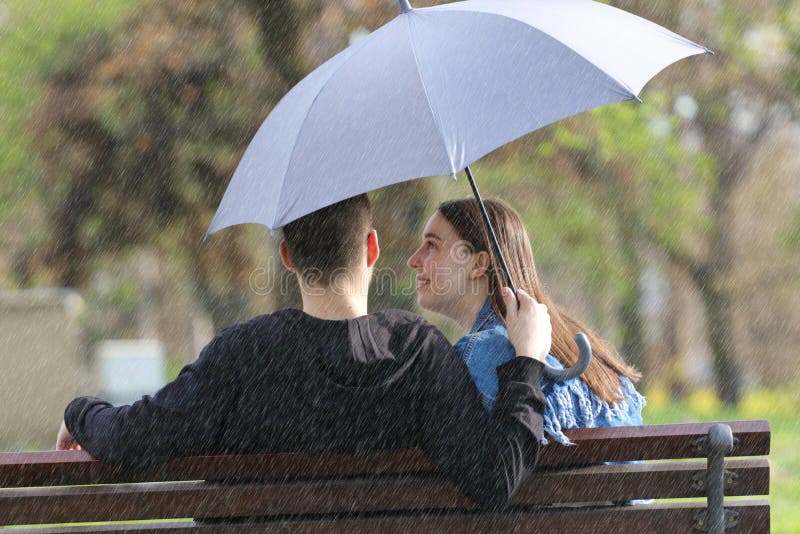 Heppy young Couple sitting on bench on the rainy spring day