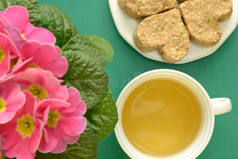 Herbal tea in cup Heart-shaped oatmeal cookies Pink flowers