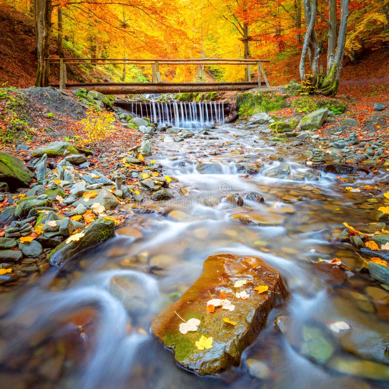 Herbstfalllandschaft - Alte Holzbrücke findet Fluss-Wasserfall in farbenfroher Herbstlandschaft - Alte Holzbrücke findet Fluss-W stockfotos