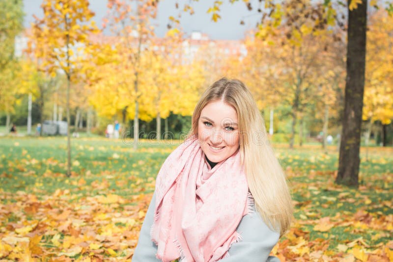 Herbstporträt im Park mit gelben Blättern eines hübschen blonden Mädchens in der warmen Kleidung und in einem rosa Schal um ihren lizenzfreies stockfoto