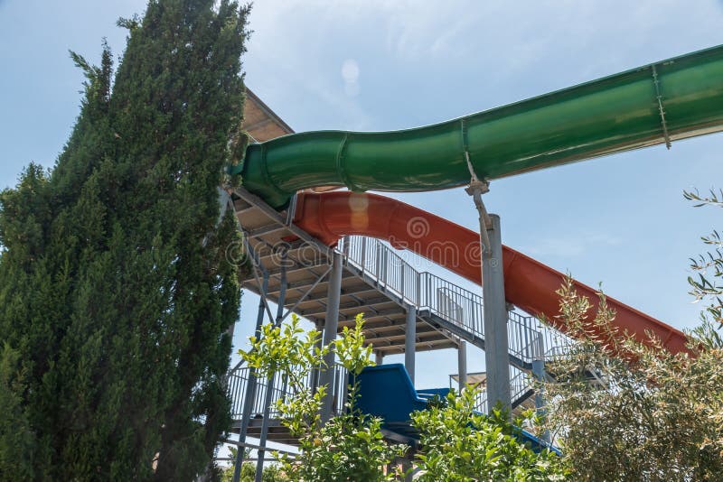 Here is the aqua park water slides. Green, red and blue water slided. Blue sky with green trees. Here is the aqua park water slides. Green, red and blue water slided. Blue sky with green trees.