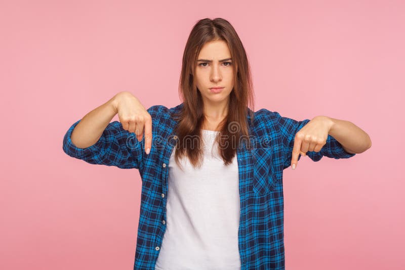 Here and right now! Portrait of demanding girl in checkered shirt pointing down, looking angrily at camera