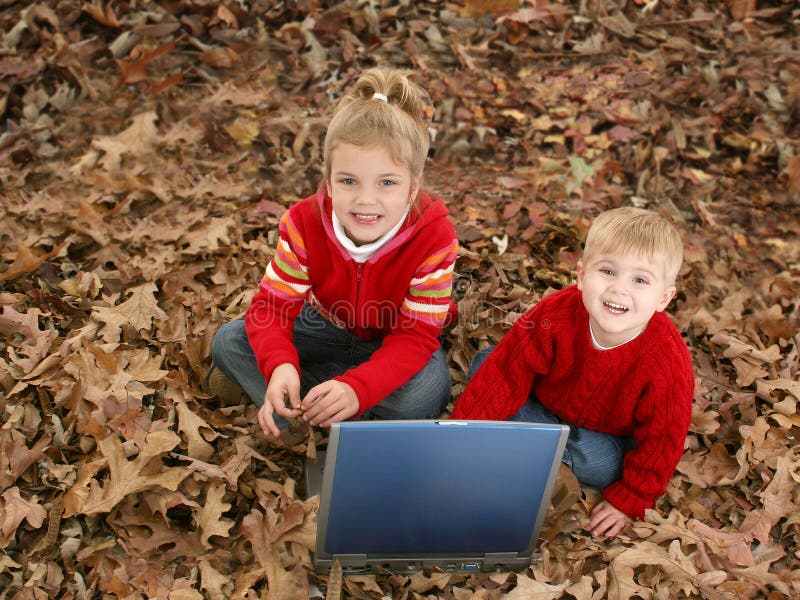 Hermano y hermana que se sientan en hojas con la computadora portátil fotos de archivo libres de regalías Hermano y hermana que se sientan en hojas con la computadora portátil fotos de archivo libres de regalías