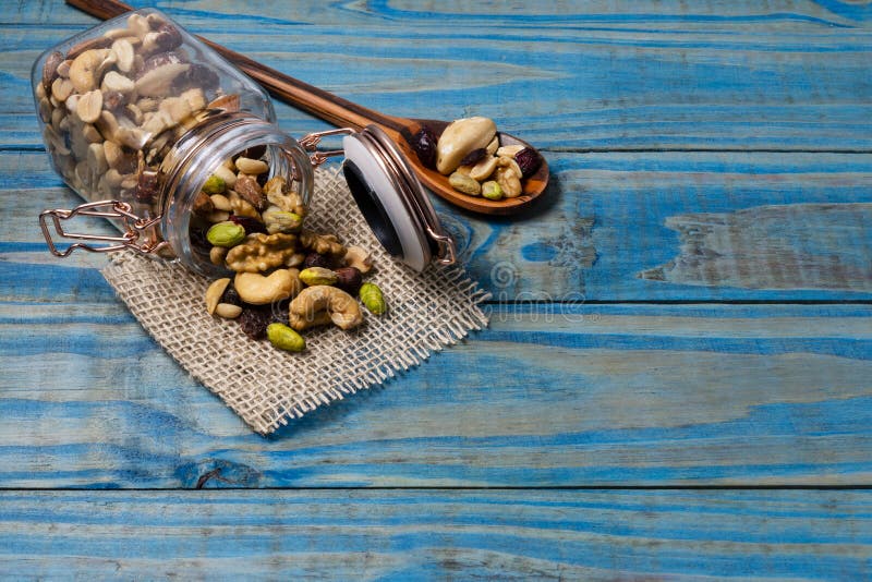 Hermetic jar of glass with mix of nuts on blue wooden table.