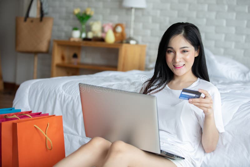 Hermosa atractiva joven asiática acostada en la cama y usando computadora portátil para usar medios sociales y comprar en línea. Hermosa y atractiva joven asiática acostada en la cama y usando ordenador portátil para usar medios sociales y comprar en línea con tarjeta de crédito relajarse en el dormitorio de vacaciones, estilo de vida en el dormitorio Concepto