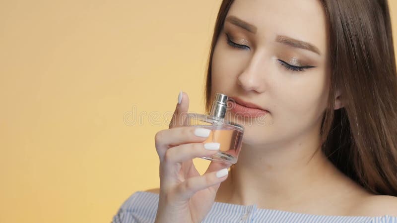 Hermosa chica sobre un fondo de color del estudio disfrutando del aroma del perfume de una botella que una joven huele y que prese