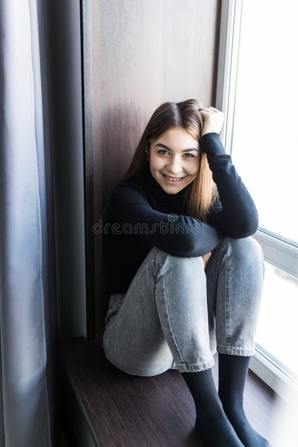 Hermosa joven sentada en casa en la ventana foto de archivo libre de regalías Hermosa joven sentada en casa en la ventana foto de archivo libre de regalías