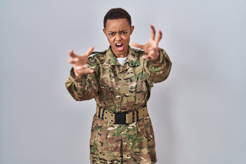 Hermosa mujer afroamericana con uniforme del ejército de camuflaje gritando frustrada con las manos furiosas tratando de estrangular a los locos