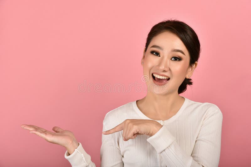 Beautiful asian woman hand open and finger point presenting product for mock-up advertising on pink background, Portrait of happy smiling girl with copy space. Beautiful asian woman hand open and finger point presenting product for mock-up advertising on pink background, Portrait of happy smiling girl with copy space
