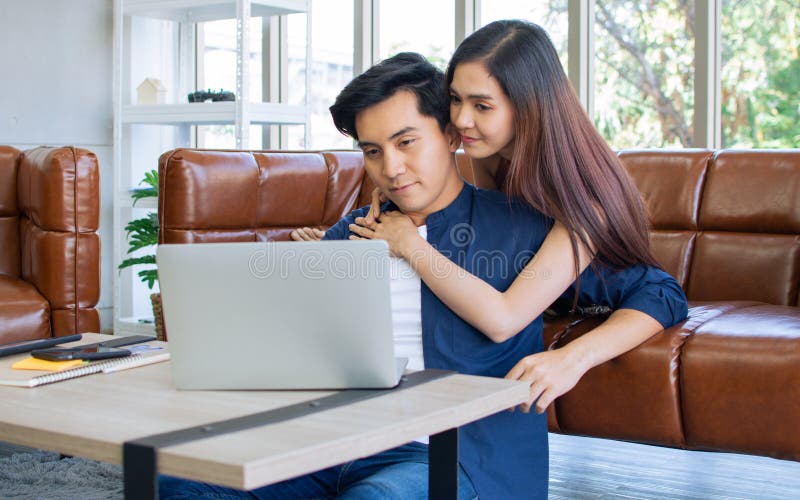 Hermosa mujer asiática sonriendo abrazando sirviendo a su amigo mientras usa una laptop para trabajar en una sala de estar en casa imágenes de archivo libres de regalías