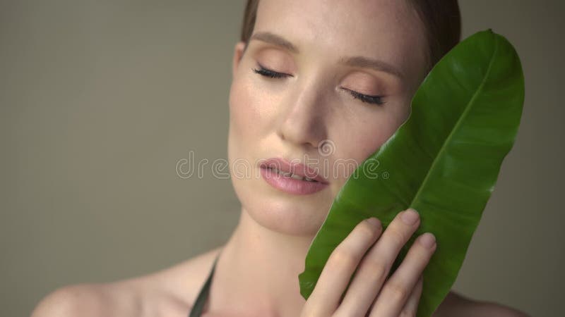Hermosa mujer con piel suave y limpia posando con hojas tropicales