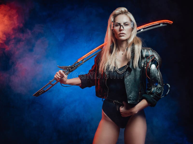 Sexy and charming woman with blond hairs in cyberpunk style poses in dark blue background holding glowing blade on her shoulder. Sexy and charming woman with blond hairs in cyberpunk style poses in dark blue background holding glowing blade on her shoulder.