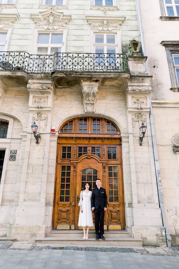 Hermosa pareja china posando cerca de la antigua puerta marrón del edificio histórico de la antigua ciudad europea fotografía de archivo libre de regalías Hermosa pareja china posando cerca de la antigua puerta marrón del edificio histórico de la antigua ciudad europea fotografía de archivo libre de regalías