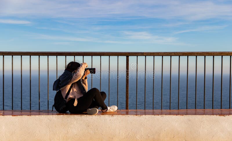 Hermosas mujeres sentadas y tomando fotos en un acantilado durante la puesta de sol imágenes de archivo libres de regalías